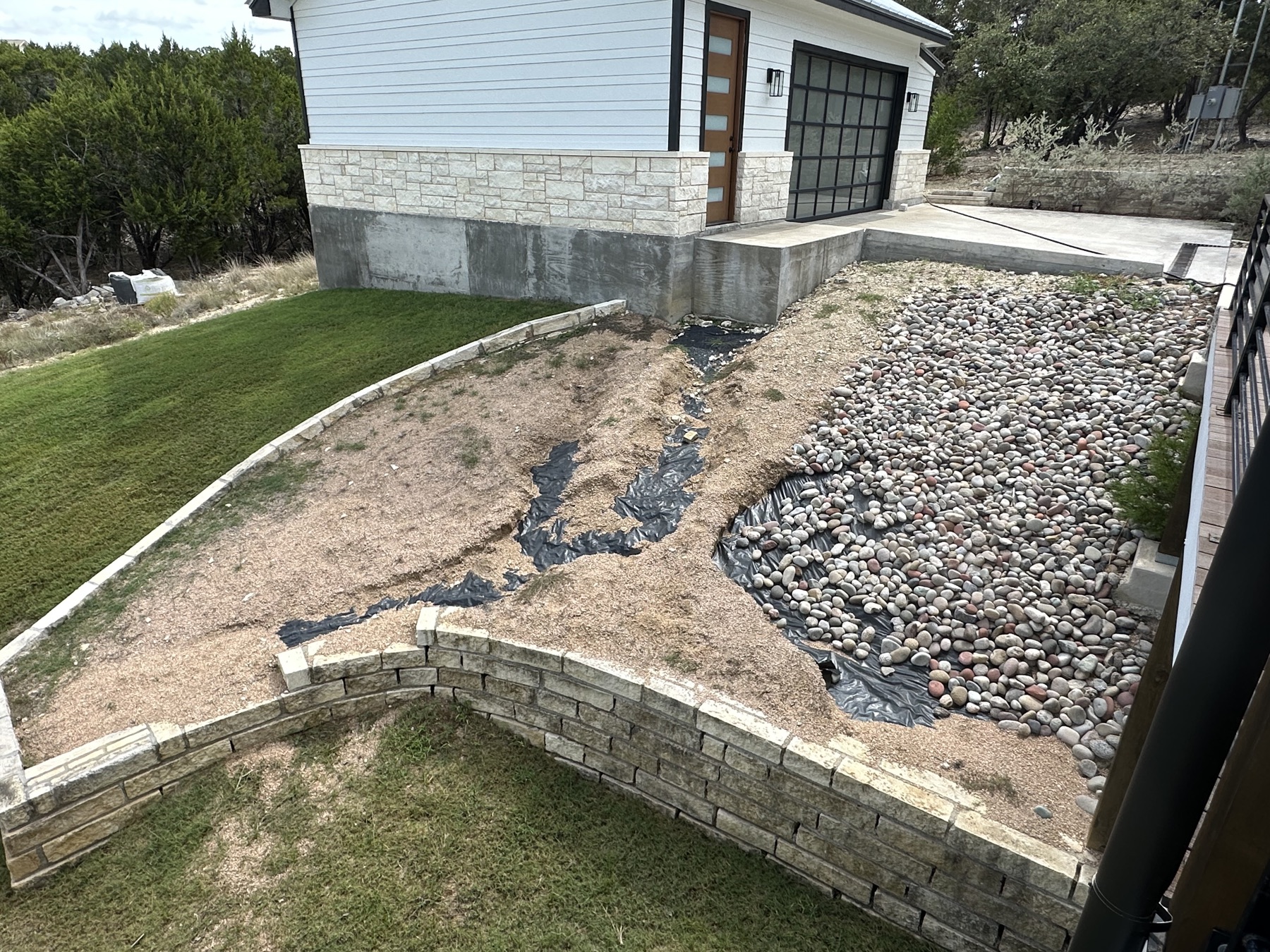 Before view of the current landscape project, with curved stone beds beside a white home